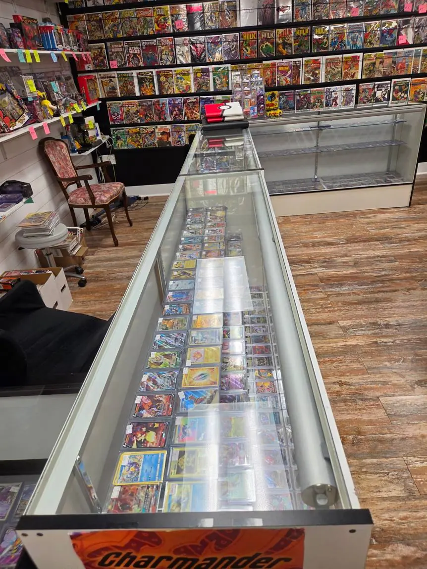 Long glass counter full of Pokémon singles and graded cards, with the vintage comic wall behind it